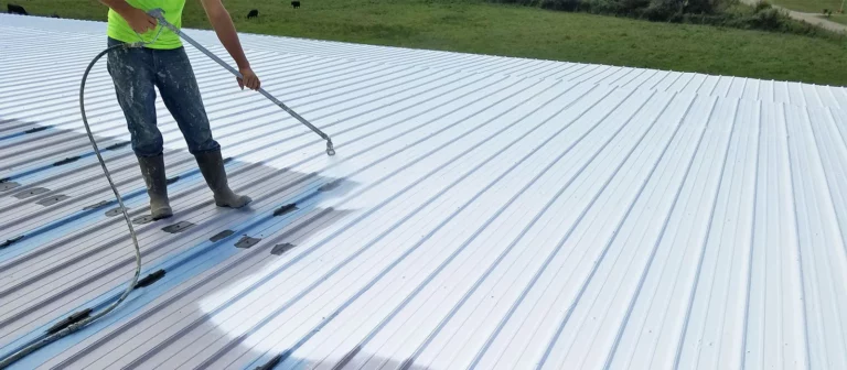 A man from a residential roofing company spraying a metal roof with a hose.