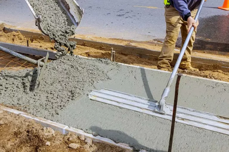 A worker from concrete contractors is pouring concrete on a sidewalk.