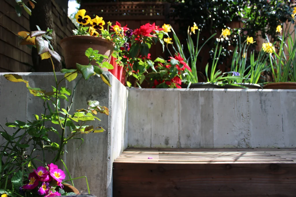 A concrete and wooden garden staircase with potted and planted flowers, including pansies and irises, in sunlight.
