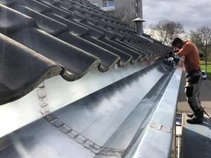 A man is working on the roof of a house with dutch gutters.