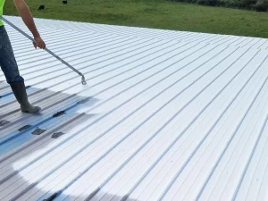 A man from a residential roofing company spraying a metal roof with a hose.