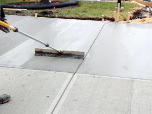 Concrete contractors are using a broom to clean a concrete sidewalk.